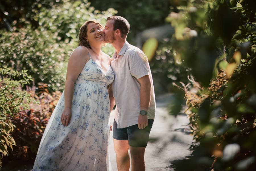 The couple shares a playful kiss surrounded by lush greenery at Brisbane Botanic Gardens.