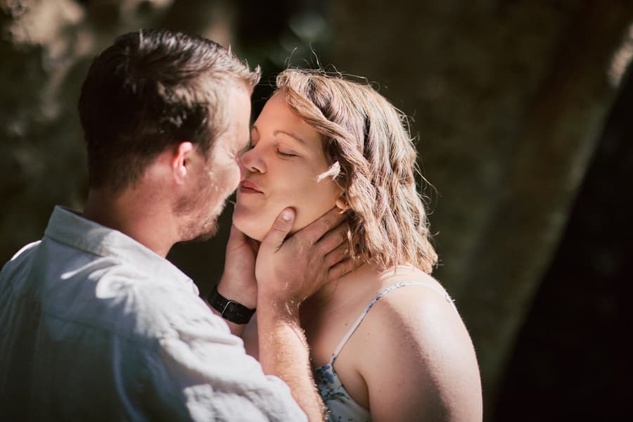 The couple shares an intimate moment, with one gently holding the other's face in soft light.