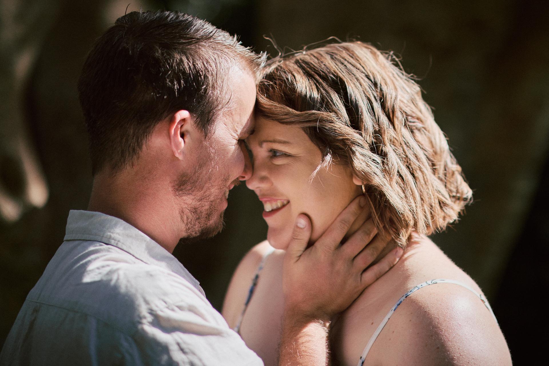 The couple gazes into each other's eyes, smiling warmly, surrounded by trees.