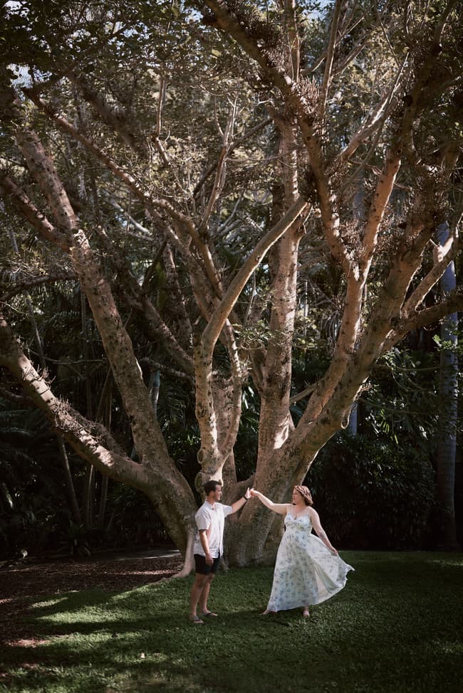 The couple dances under a large tree, sunlight filtering through the branches.