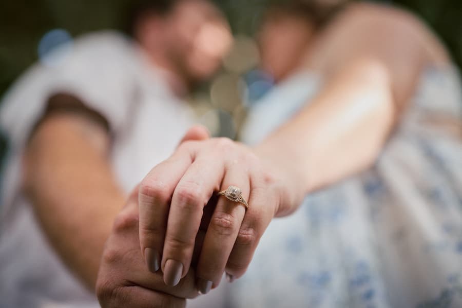 Close-up of the couple holding hands, focus on the engagement ring, blurred background.
