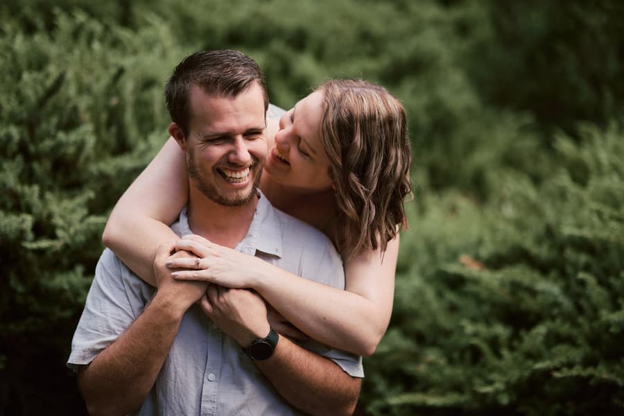 The couple shares a joyful hug, one wrapping arms around the other from behind.