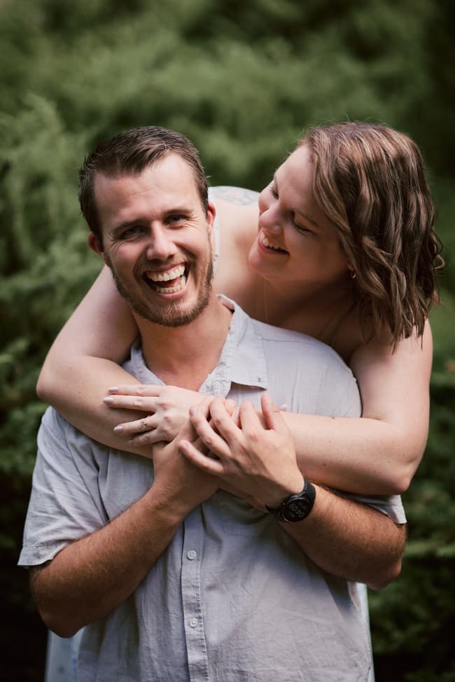 The couple laughing joyfully, with one embracing the other from behind, surrounded by lush greenery at Brisbane Botanic Gardens.