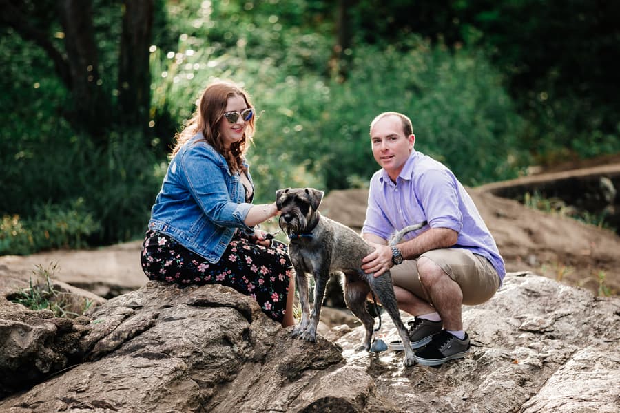 The couple kneels on rocks with their dog at Merv Ewart Reserve, surrounded by greenery.