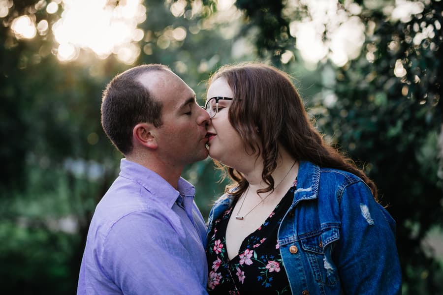 The couple shares a kiss with trees softly blurred in the background at Merv Ewart Reserve.