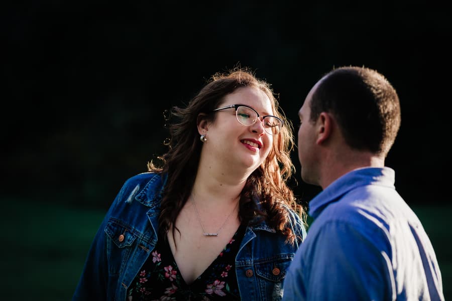Close-up of the couple smiling at each other, with greenery in the background.