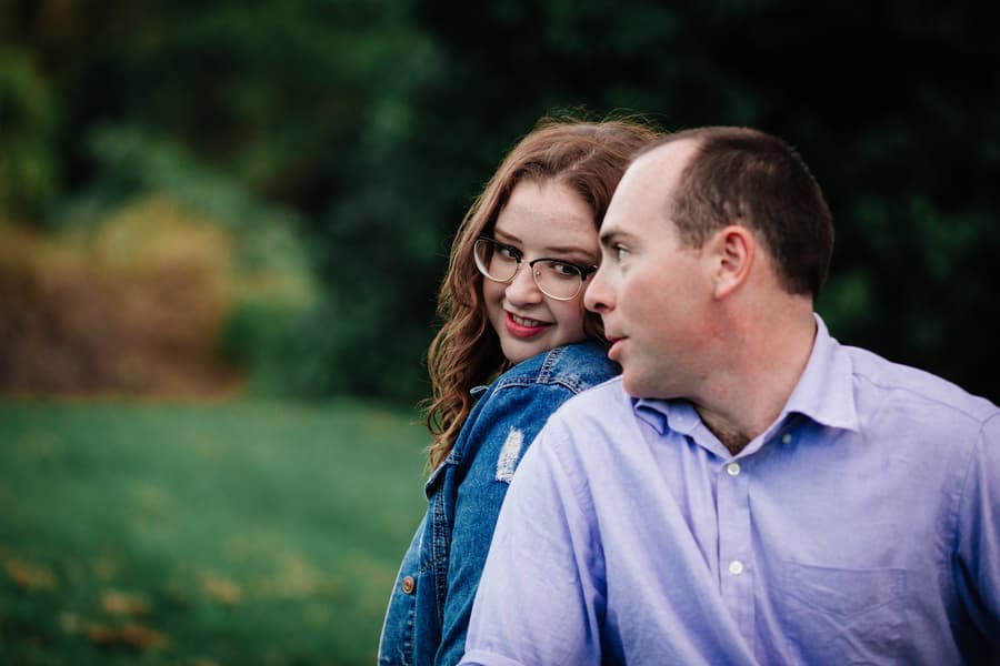 The couple sits closely, sharing a moment of connection in a green park setting.