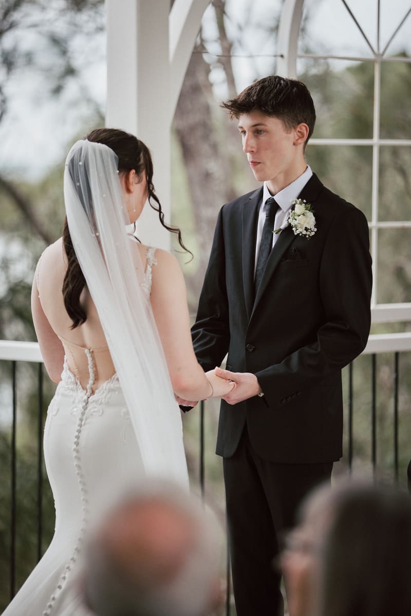 Terion the bride and Tyler the groom hold hands facing each other during their wedding ceremony. Winter wedding Brisbane dress code by She Said Yes.