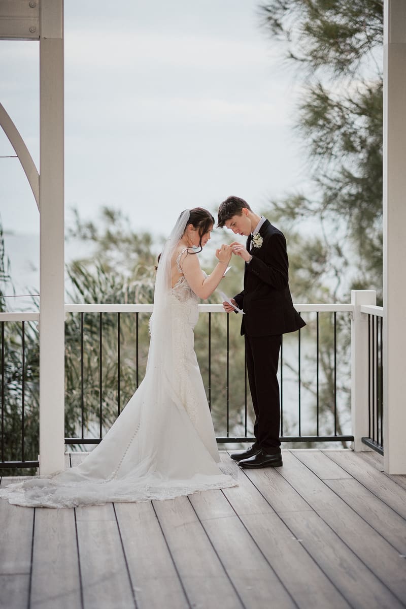 The bride Terion and groom Tyler stand on a wooden deck, holding hands and looking down at their joined hands in a tender moment during their couple portraits session. Marriage equality Australia by She Said Yes.