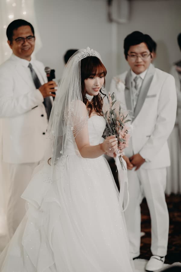 The bride Henny holds a bouquet during the ceremony at Royal on the Park, with the groom Timothy and an officiant standing nearby.