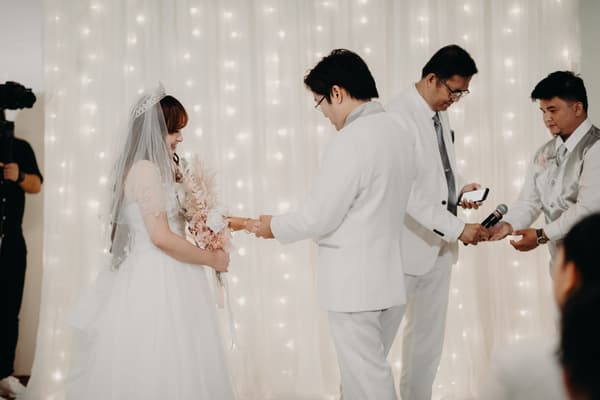 Bride Henny and groom Timothy exchange rings during their wedding ceremony at Royal on the Park, with an officiant and a groomsman assisting nearby.