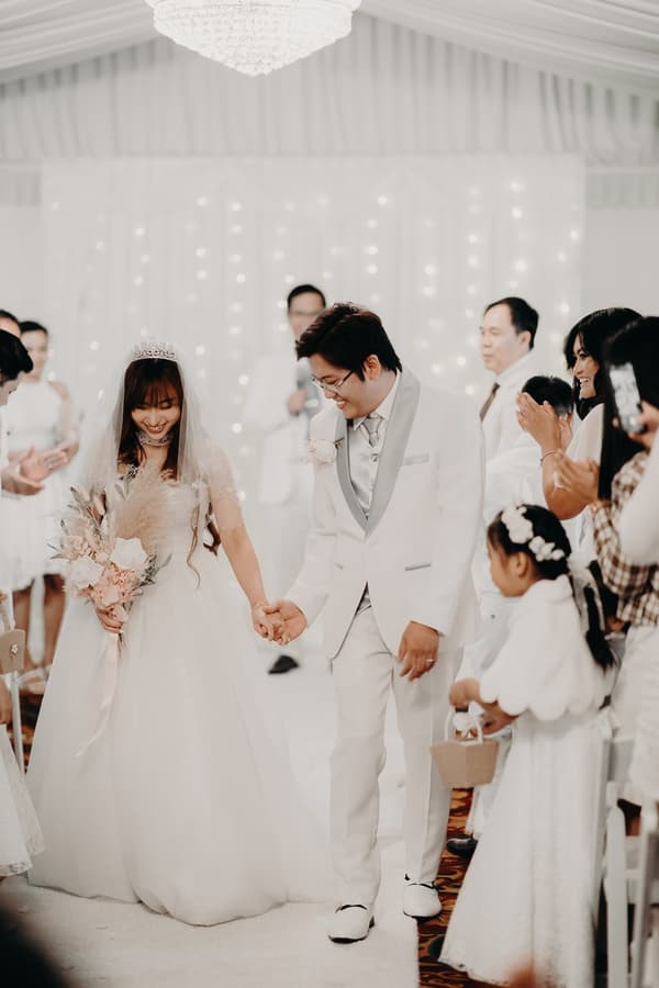 Bride Henny and groom Timothy hold hands and walk down the aisle at Royal on the Park, surrounded by applauding guests and a flower girl holding a basket.