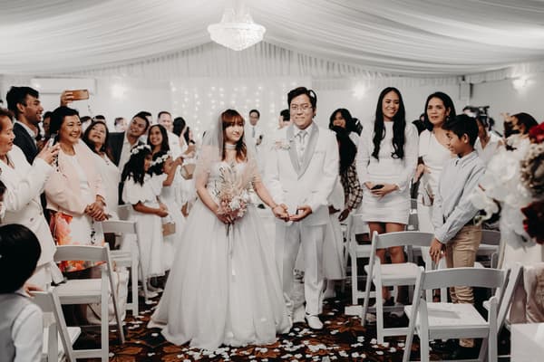Bride Henny and groom Timothy walk down the aisle together at Royal on the Park, surrounded by seated and standing guests who are watching and taking photos.