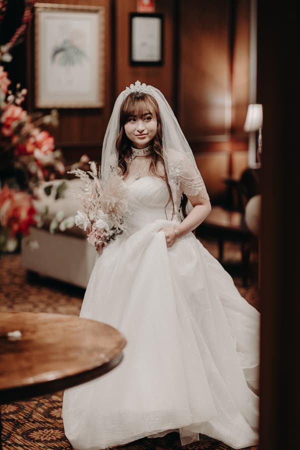 The bride Henny stands indoors at Royal on the Park wearing a white wedding gown and veil, holding a bouquet of dried flowers.