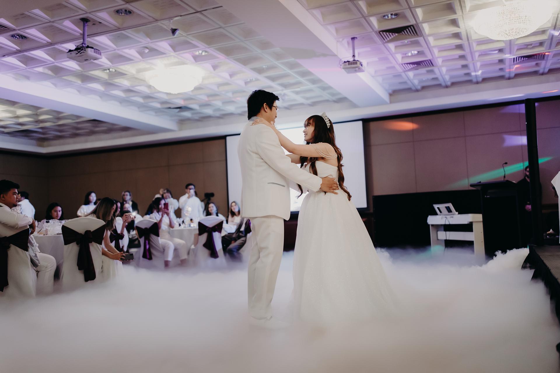 Timothy and Henny share their first dance surrounded by seated guests at the reception in Royal on the Park, with low fog covering the dance floor.