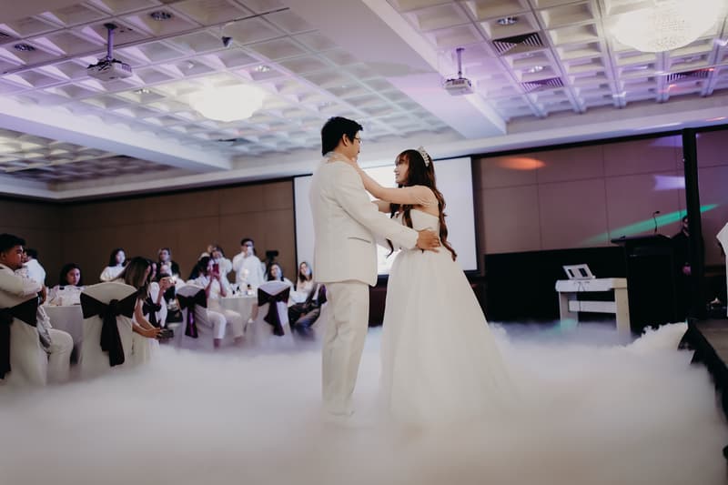 Timothy and Henny share their first dance surrounded by seated guests at the reception in Royal on the Park, with low fog covering the dance floor.