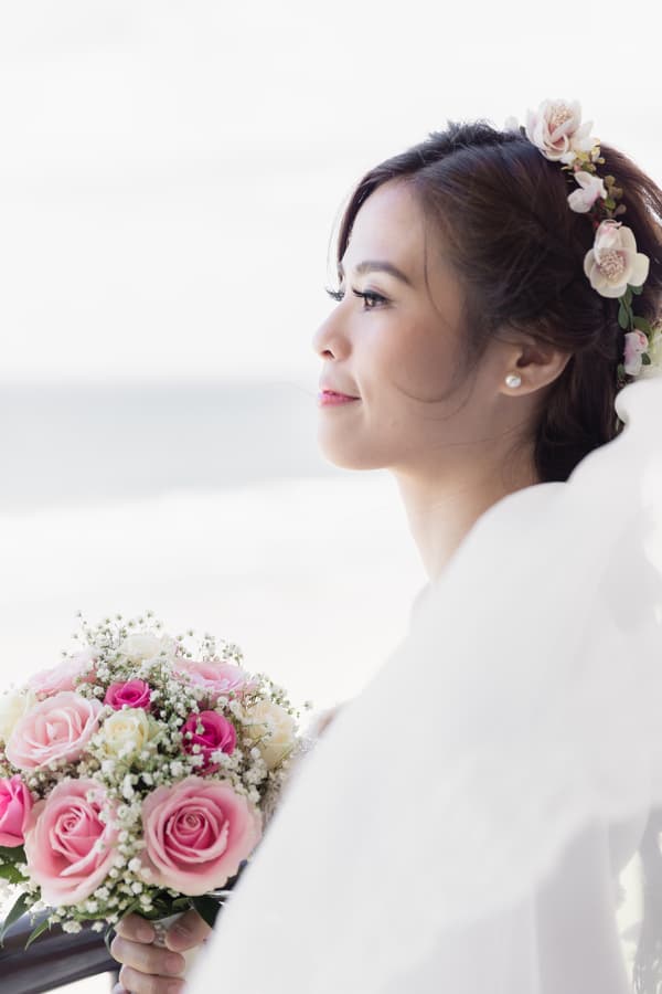 The bride Wing holds a bouquet of pink and white roses with baby's breath at Bilinga Beach Weddings during a couple portrait session.