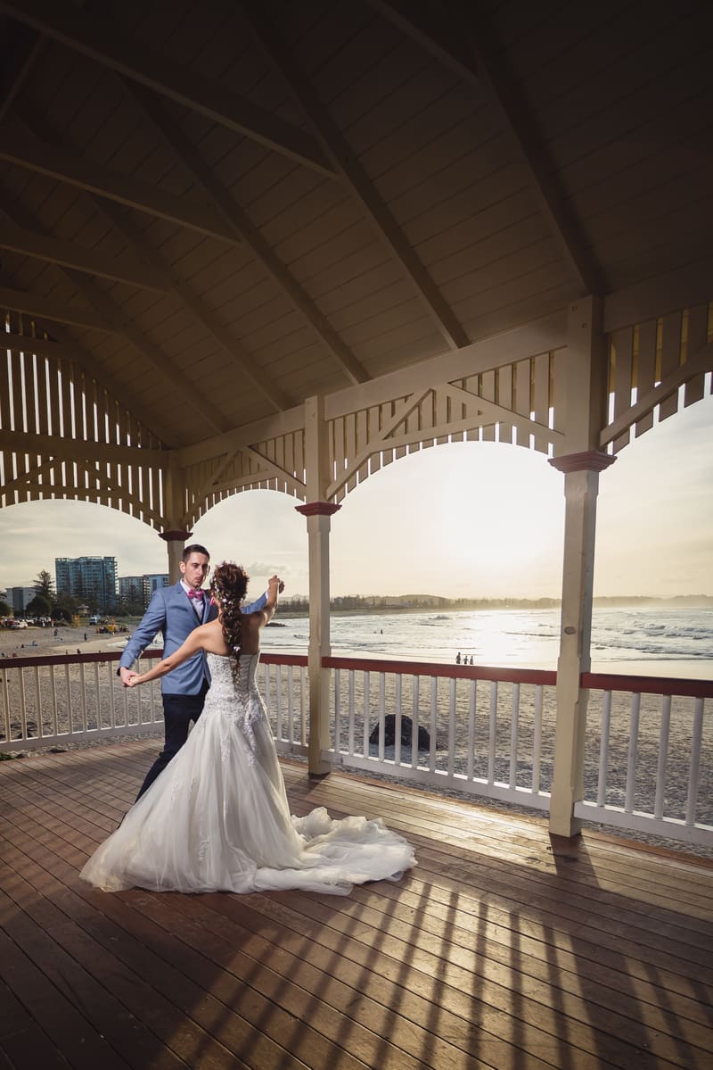 The bride and groom dance together under a wooden pavilion overlooking the beach. Bridal editorial photography by She Said Yes.