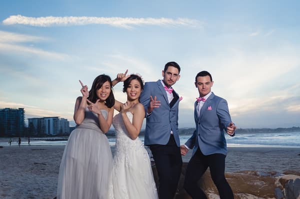 The bride Wing and groom Jason pose with a bridesmaid and a groomsman on the beach. Brisbane videographer by She Said Yes.