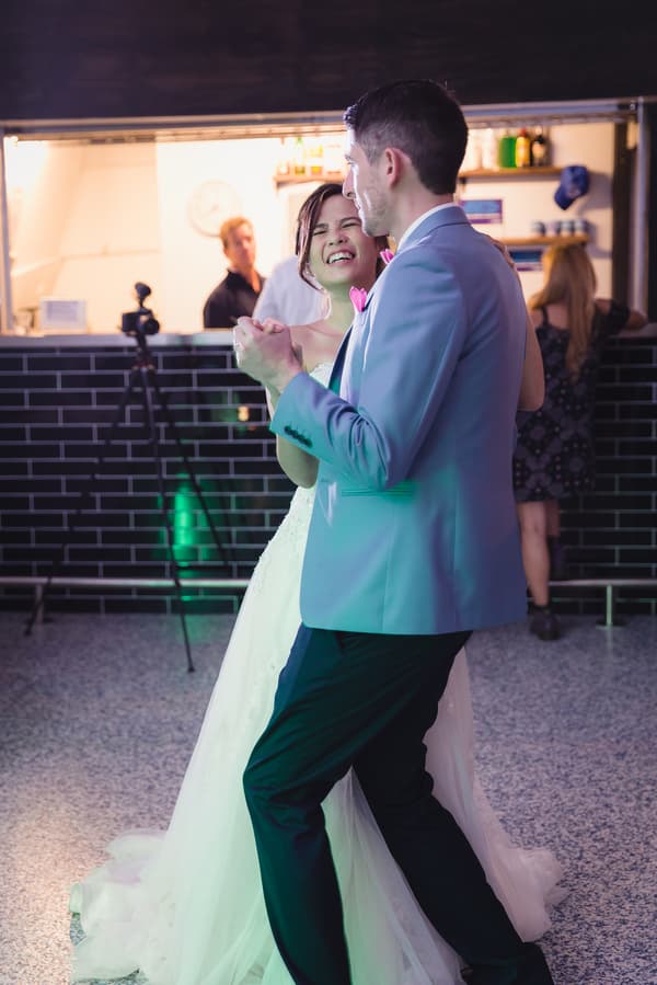 Bride Wing and groom Jason dance together at the reception stage of Bilinga Beach Weddings — Bilinga SLSC, with guests and a bar area visible in the background.