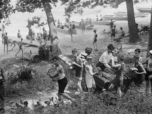 Group of Boys carry loaves of bread from wagons near beach front in woods. - Art Print
