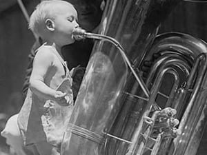 An nearly naked infant toots a tuba many times his size - Art Print
