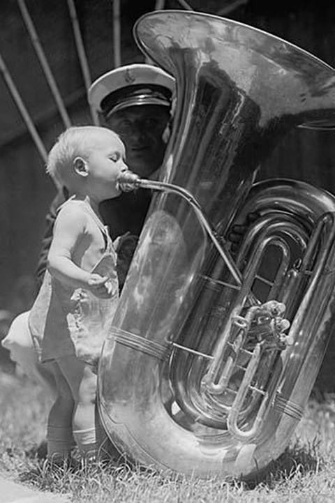 An nearly naked infant toots a tuba many times his size - Art Print