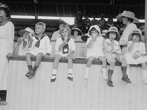 Children sit on wall in front of stands at the ballpark and eat ice cream cones. - Art Print