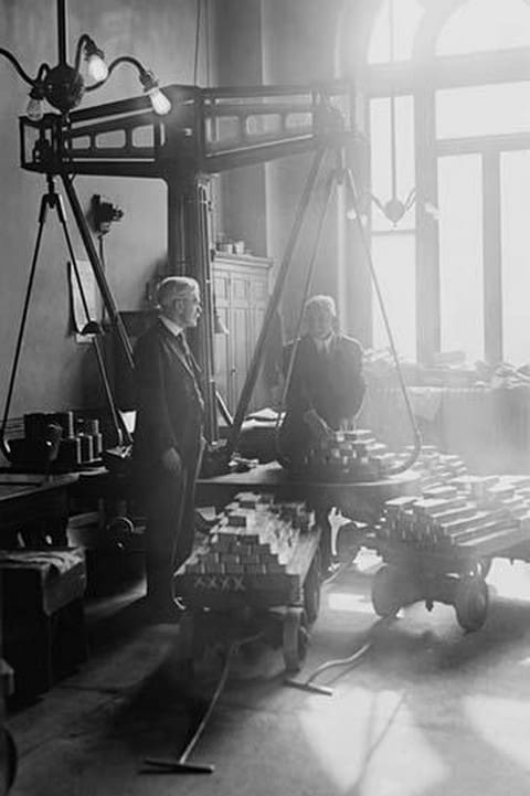 Two suited men weigh bars of gold on scales at the US Mint - Art Print