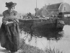 A Older Dutch woman has a bustle around her chest as she pulls a barge down a canal. - Art Print