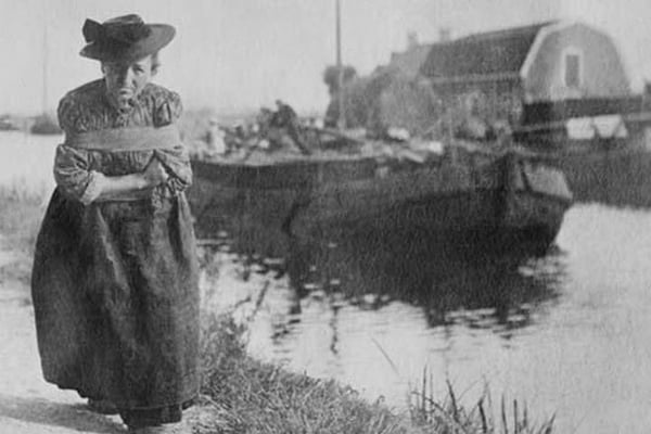 A Older Dutch woman has a bustle around her chest as she pulls a barge down a canal. - Art Print