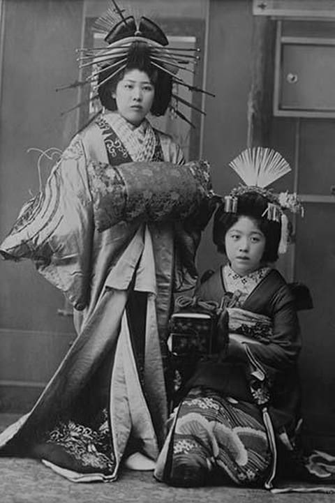 Two Young Beautiful Japanese Geishas accoutered in the ceremonial costumes and hairstyles of ancient Japan with Kimono