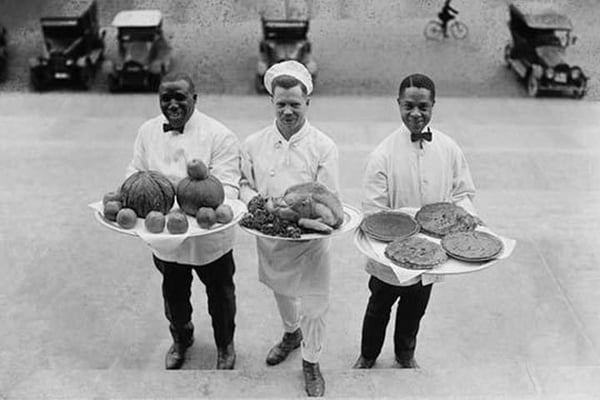 Three Chefs stand on bottom of a line of steps and hold up Thanksgiving platters of Pies