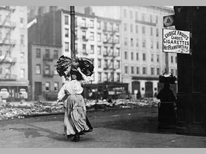 Immigrant Woman Walks Down Street Carrying a Pile of Clothing on Her Head - Art Print