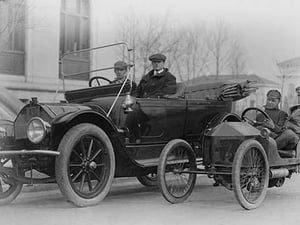 Two men in a large auto are side by two men in a Miniature Auto - Art Print