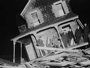 Men stand on Porch of a Sea bright Cottage torn from its foundation and tilted at a 45 degree angle. - Art Print