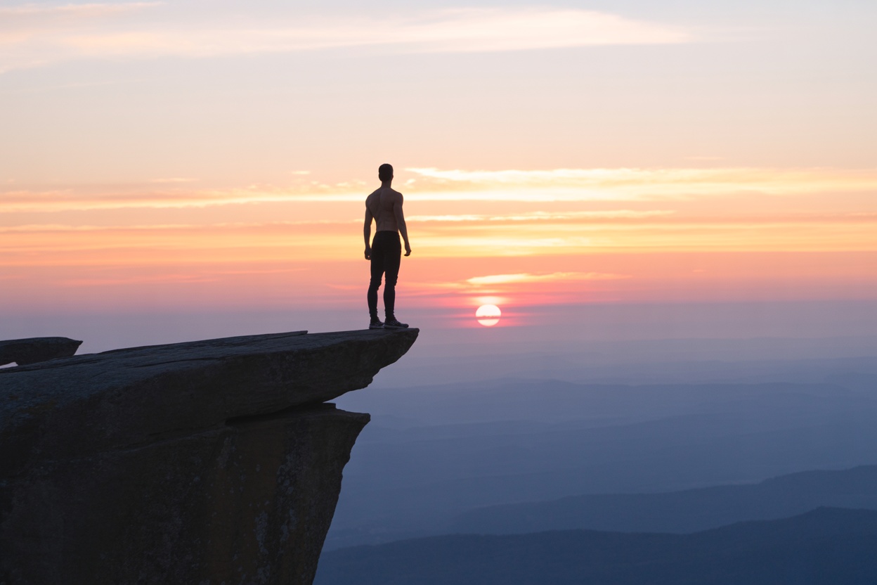 A person standing on a cliff with a sunset, symbolizing personal growth and the future.