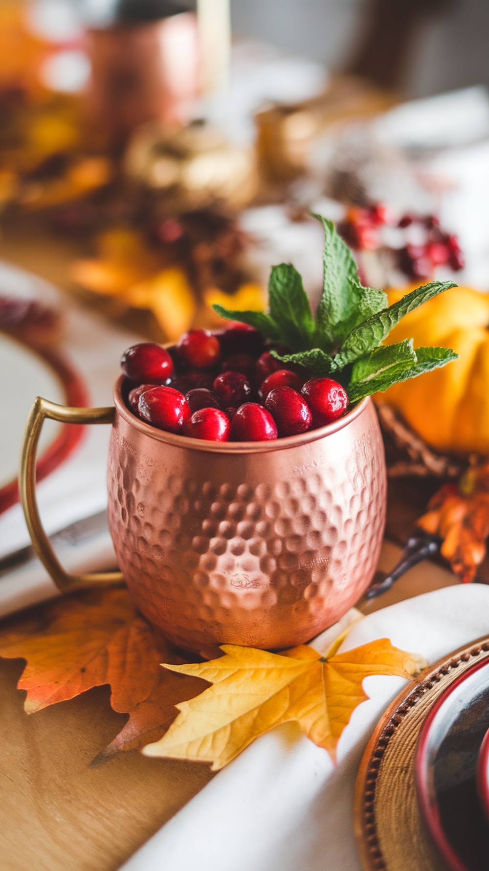 A copper mug filled with cranberries and mint leaves, surrounded by autumn leaves and festive decor.