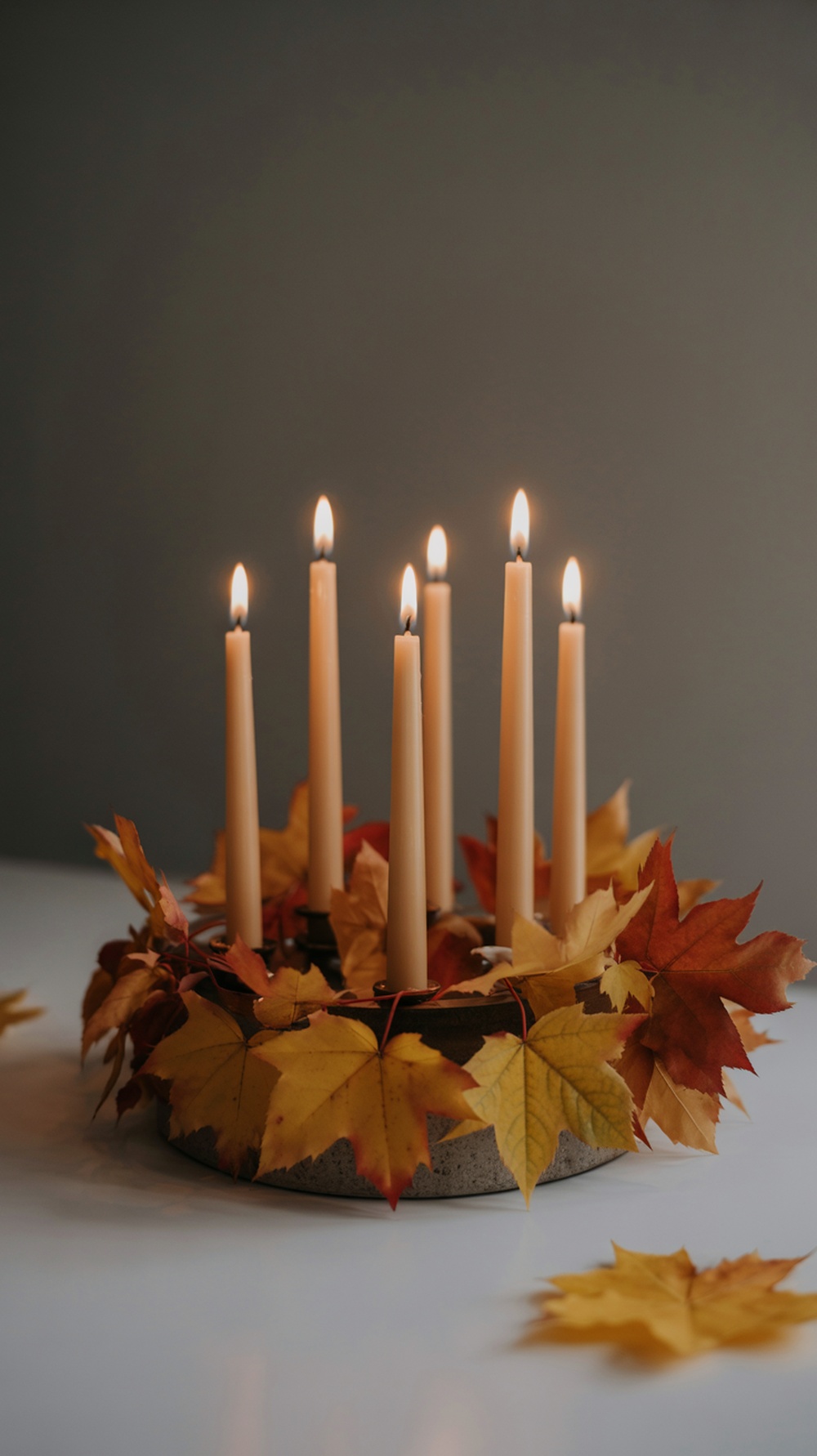 A fall centerpiece featuring candles surrounded by colorful autumn leaves.