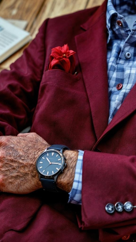 A close-up of a maroon blazer with a checkered shirt, featuring a red pocket square and a stylish watch.