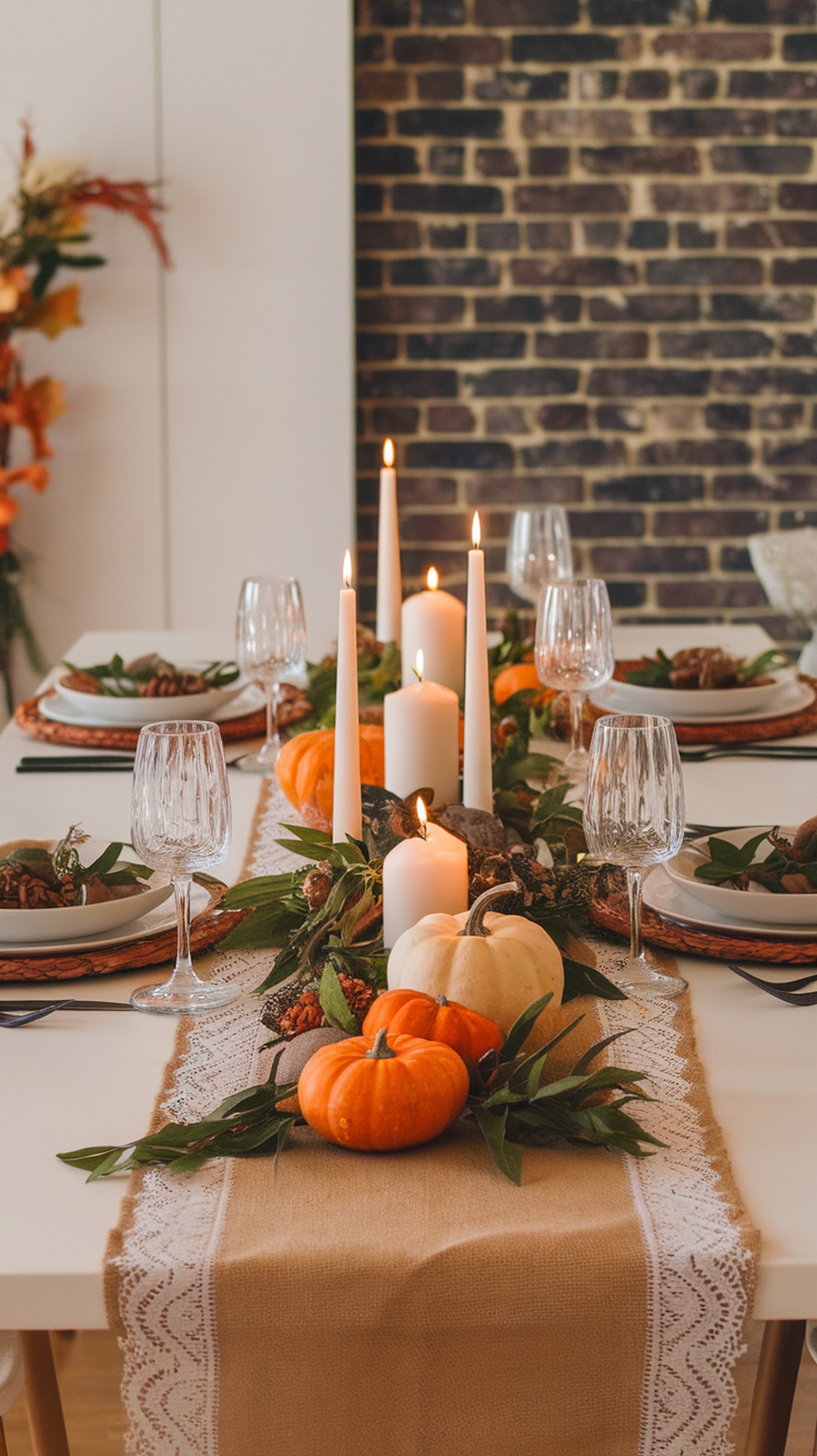 A table set with a burlap and lace runner, pumpkins, candles, and elegant glassware.