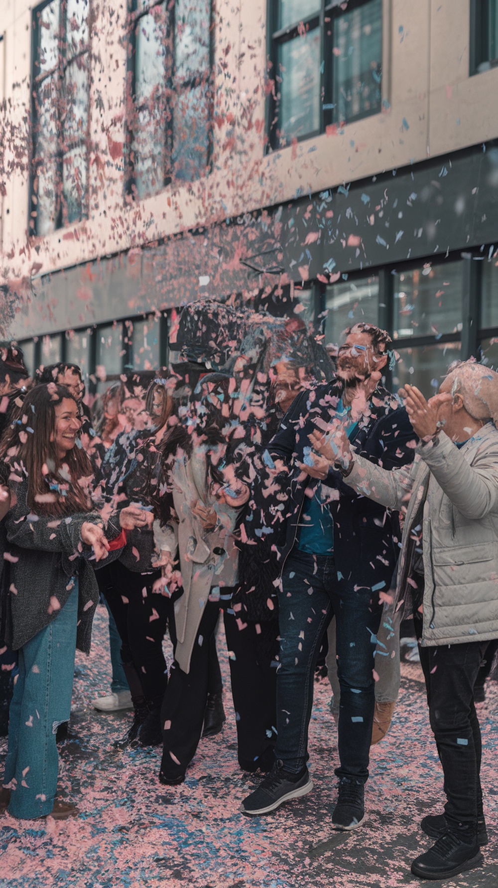 A group of people celebrating a gender reveal with confetti cannons, surrounded by colorful confetti.