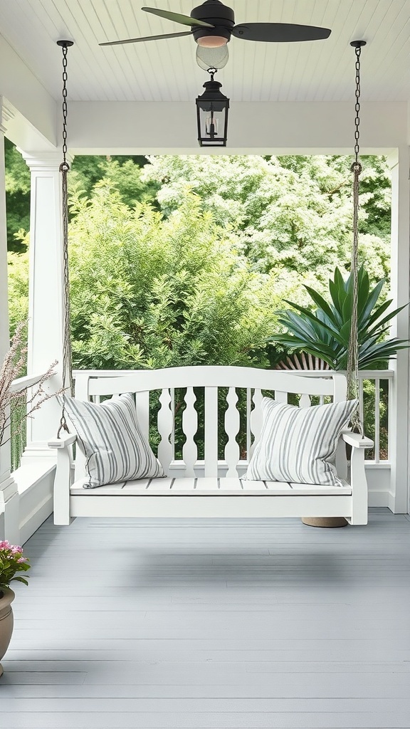 A cozy white porch swing with striped pillows, surrounded by greenery and a ceiling fan above.