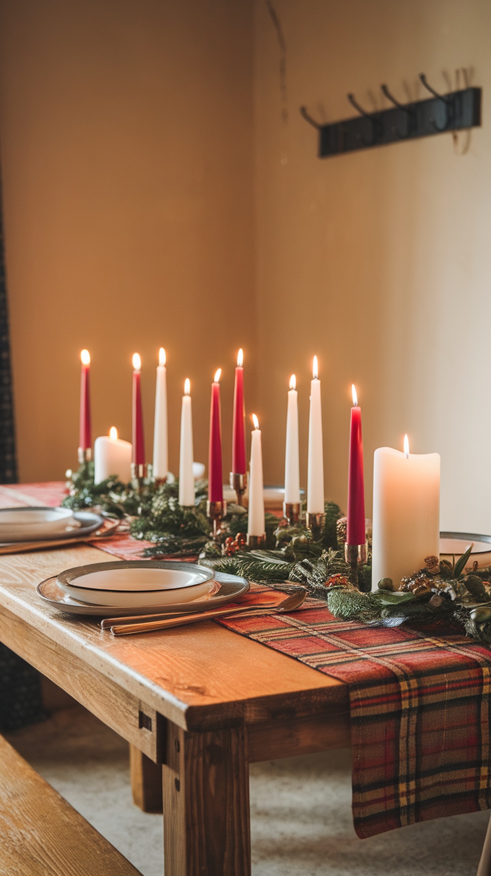 A wooden dining table with a plaid table runner, candles, and greenery for Christmas decor.