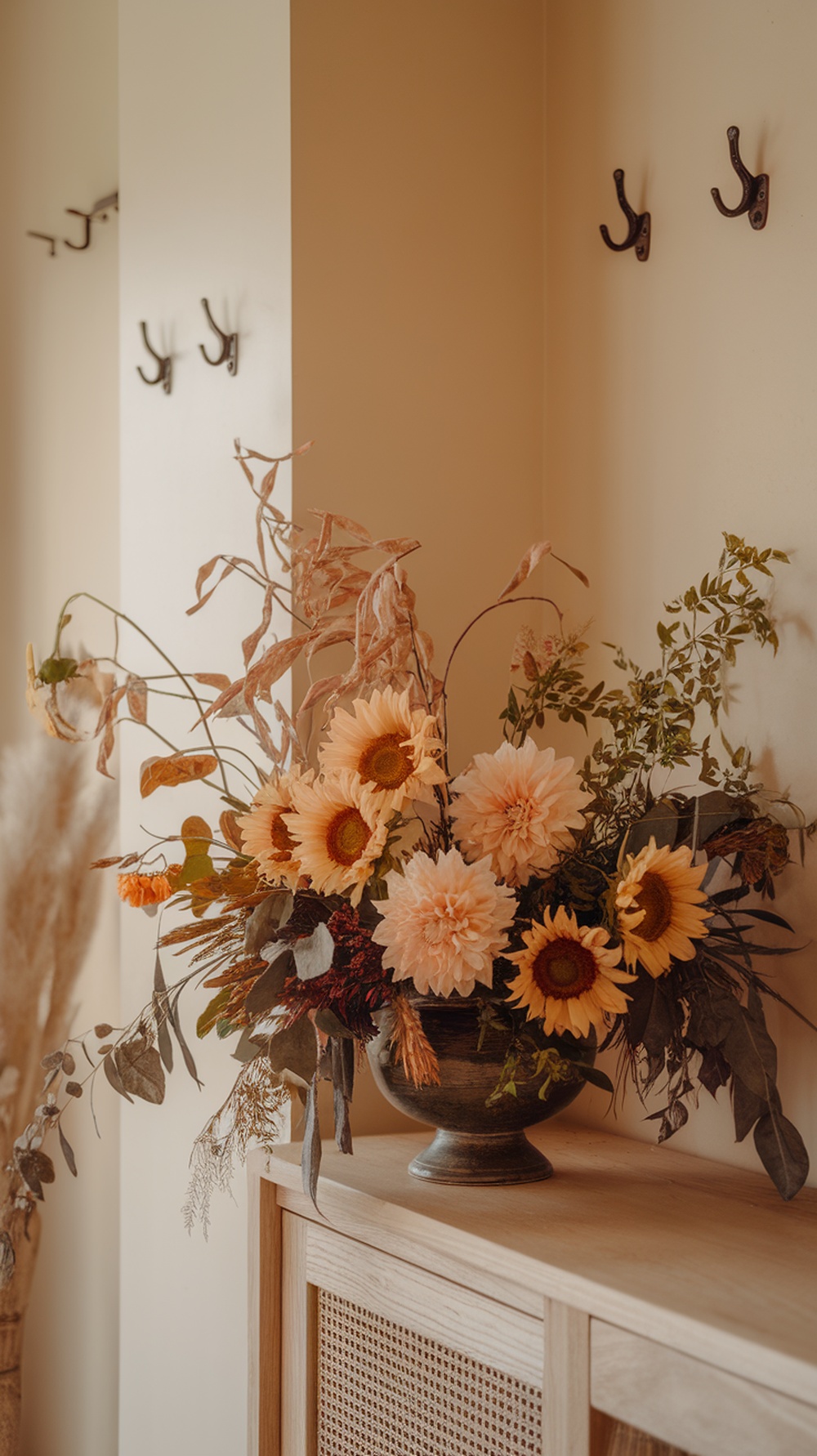 A floral arrangement featuring sunflowers and dahlias in a decorative vase, set against a warm-toned wall.