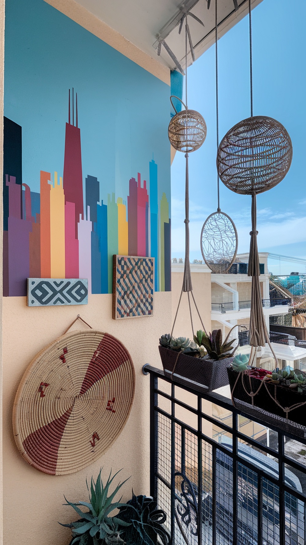 A balcony featuring a colorful city skyline mural, woven wall art, and hanging plants.