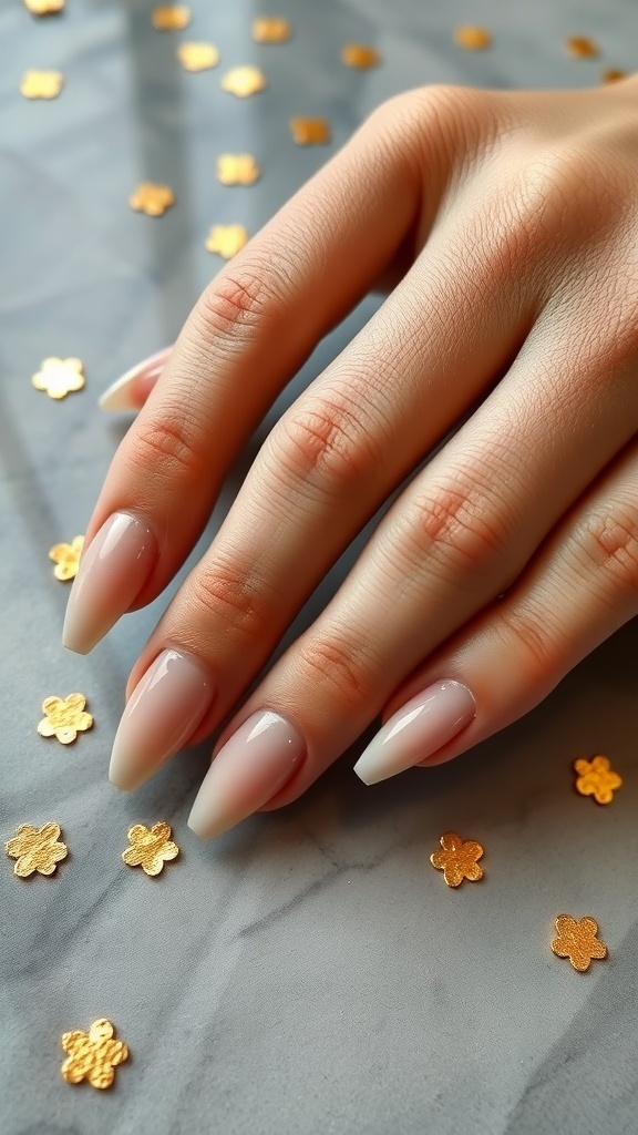 Close-up of manicured nude nails with a glossy finish and gold flower accents on a marble surface.