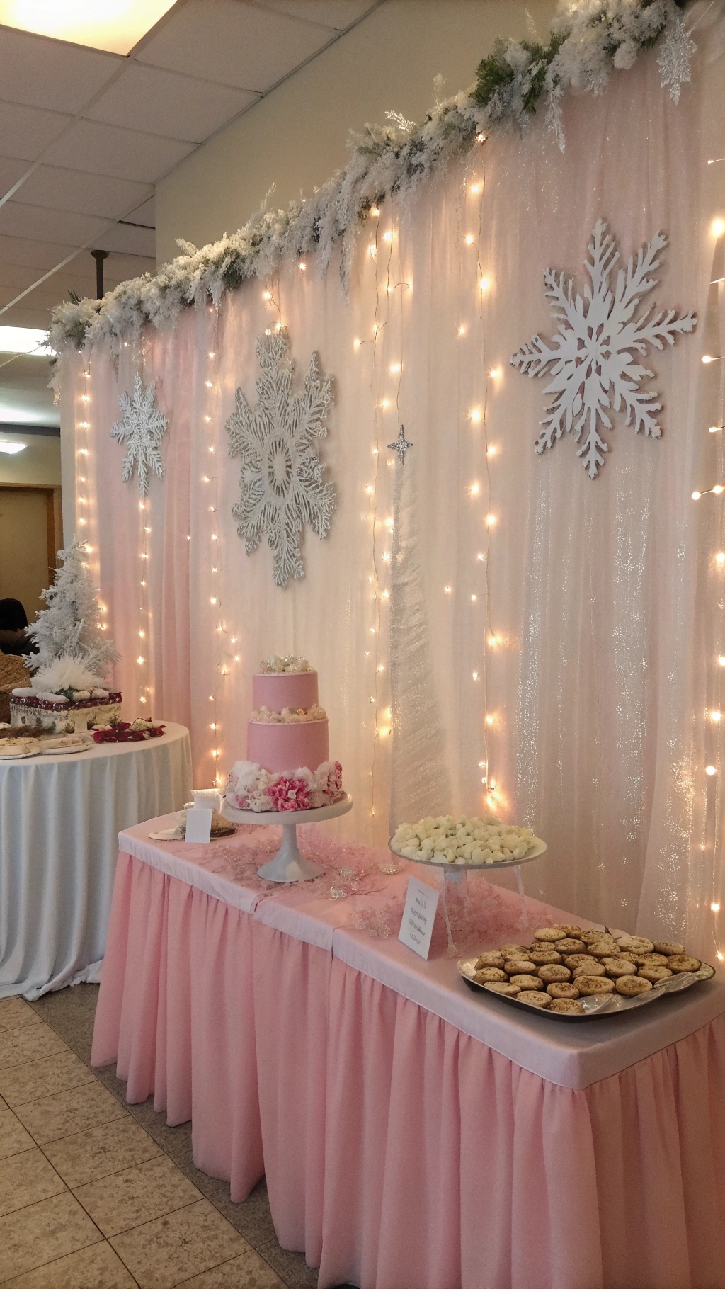 A pink winter wonderland baby shower setup with a shimmering backdrop, snowflakes, and a dessert table.