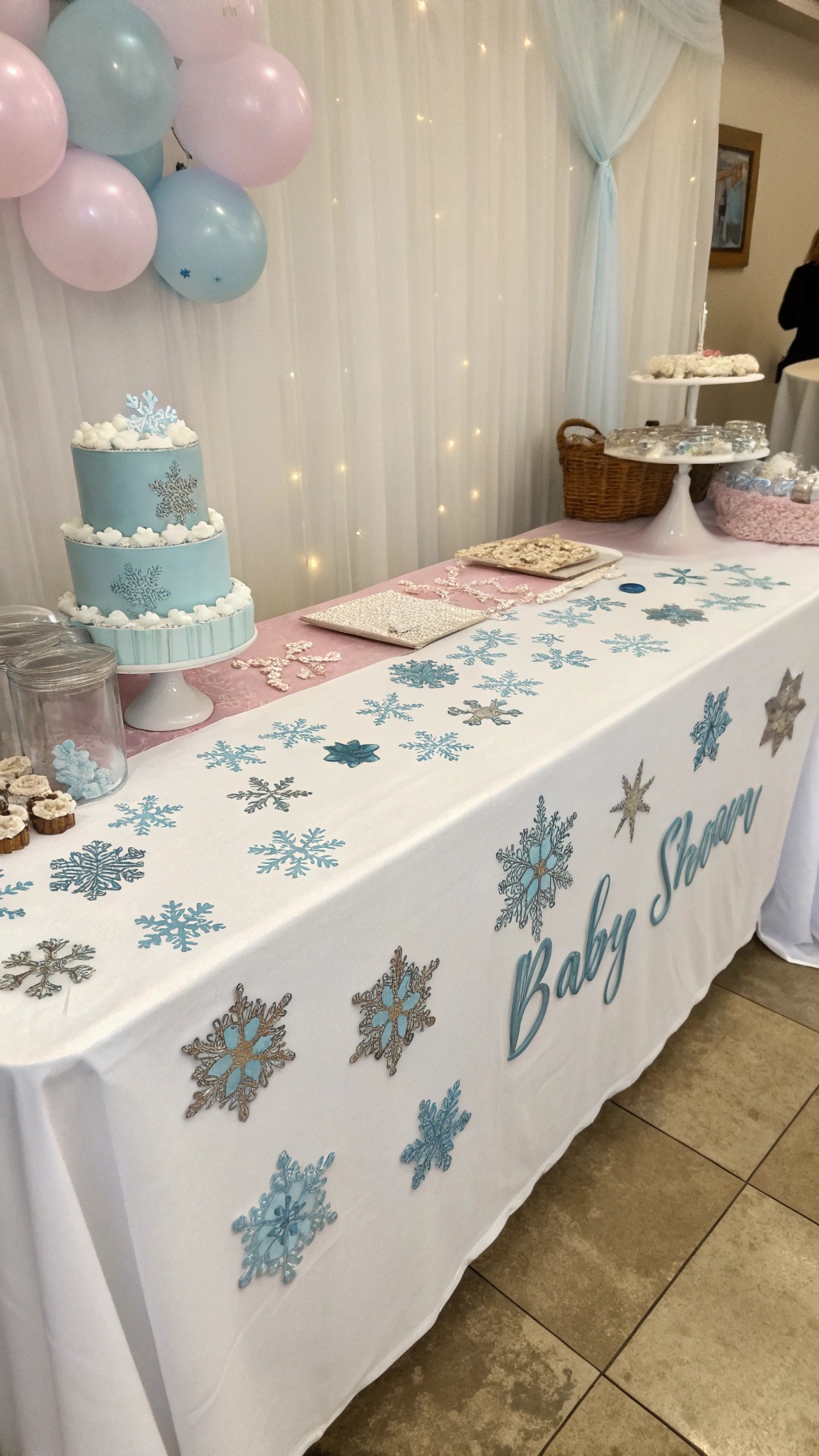 A table decorated with snowflake confetti, a blue cake, and treats for a baby shower.