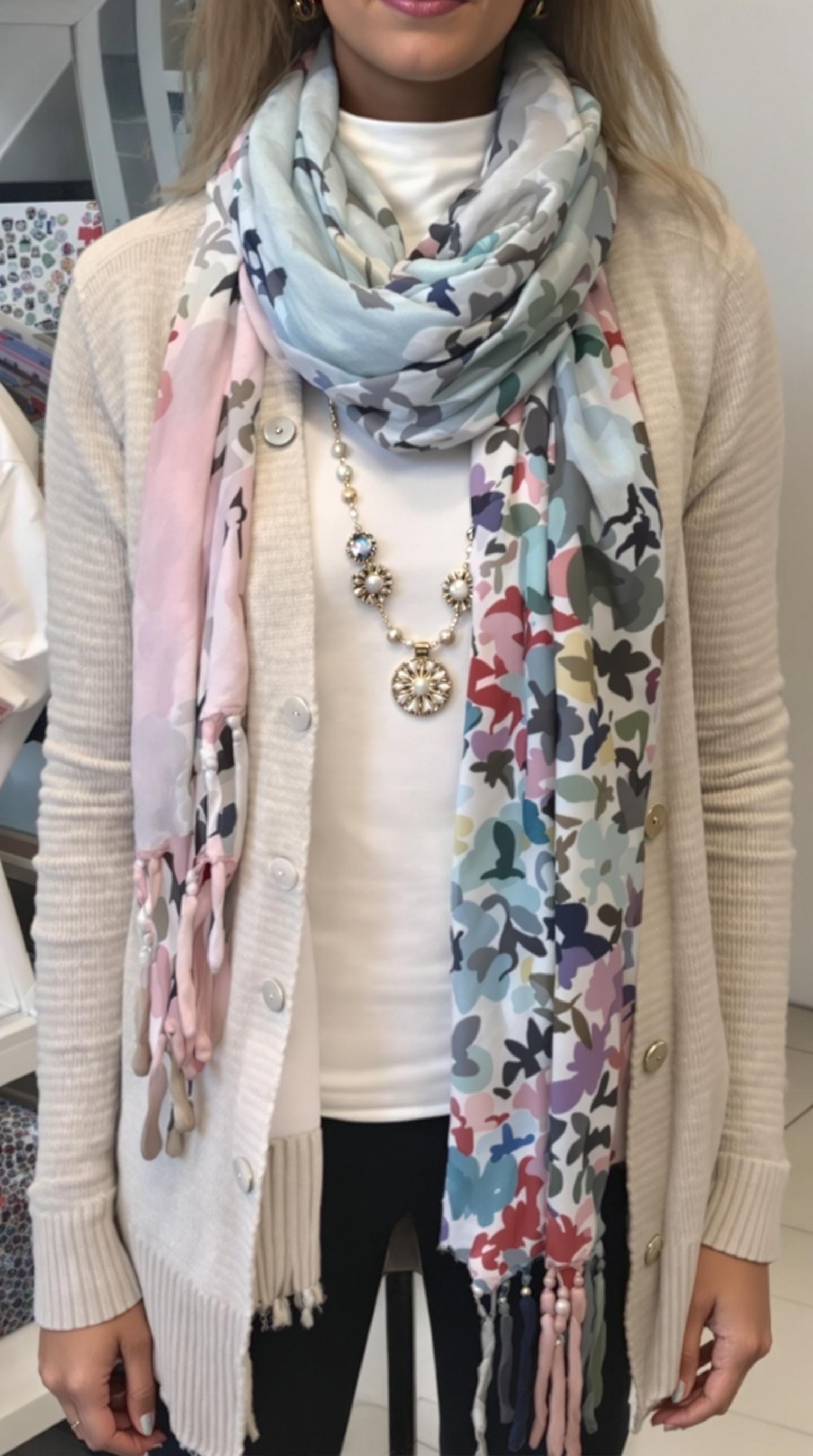 A beige cardigan displayed with a colorful scarf and a statement necklace on a mannequin.